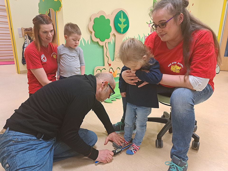 Wieland Kinz von kinderfuesse.com misst in der DRK-Kita Bummi in Gielsdorf die Füße von Katharina. Die Erzieherinnen Karina Pruskil (mit Ben) und Sabrina Janik (von links) schauen zu. 